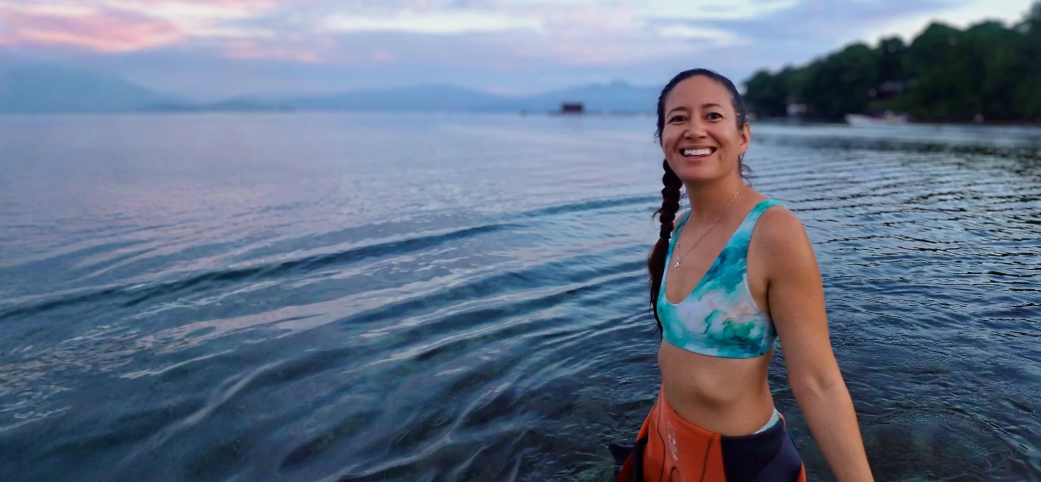 Woman standing by a lake with braided hair and a Turquoise scuba bikini getting ready for a dive 